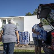 Muž na snímku nakládá balenou pitnou vodu do auta, zatímco k distribučnímu centru v louisianském kostele Trinity přijíždějí další lidé. Foceno 17. října.