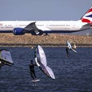 Skupina surfařů a letadlo British Airways na mezinárodním letišti v Sydney za větrného australského jarního dne. Foceno 4. září.