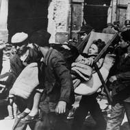 Příbuzní nesou těžce nemocnou ženu na lehátku po neúspěchu Varšavského povstání, 18. října 1944.  