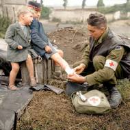 Kanadští vojáci  během postupu v Normandii v roce 1944. vojín J. W. Curtis z Královského kanadského armádního lékařského sboru ošetřuje zranění malého francouzského chlapce. Vyfoceno pravděpodobně v Bernières-sur Mer. Vylodění v Normandii se zúčastnilo v řadách spojenců 14 tisíc kanadských vojáků, přes tisíc jich zahynulo.
