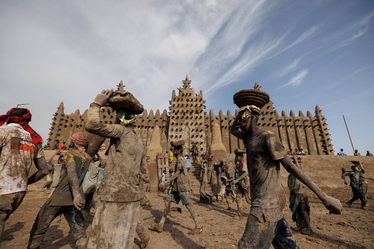 Za rytmu bubnů a veselé hudby pokryli obyvatelé města Djenné mešitu čerstvou hliněnou omítkou, aby opravili poškození, jež na mešitě během roku zanechaly déšť a eroze.
(Lidé nesou na hlavách kbelíky plné bláta, 12. červne v Djenné.)