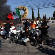 Někteří demonstranti nesli mexické vlajky a měli nasazené roušky. Na místě hořely barikády i auto, jak je vidět na snímku z losangeleské čtvrti Paramount.