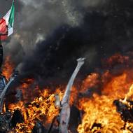 Demonstrant mává mexickou vlajkou před hořícími auty během protestu proti federálním imigračním kontrolám v centru Los Angeles.