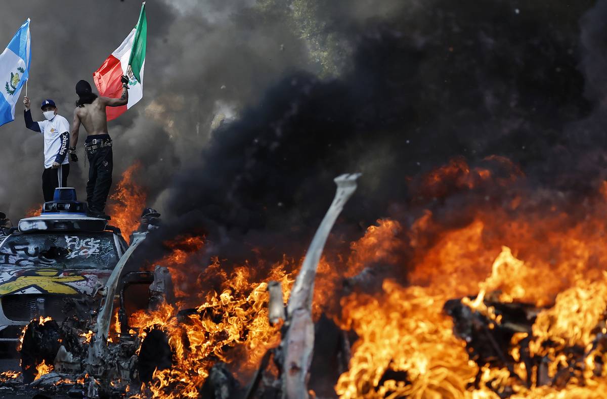 Demonstrant mává mexickou vlajkou před hořícími auty během protestu proti federálním imigračním kontrolám v centru Los Angeles.