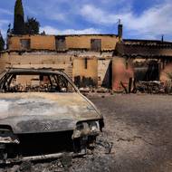 Zničený automobil stojí poblíž domu poškozeného lesním požárem v Saint-Laurent-de-la-Cabrerisse nedaleko Narbonne v jižní Francii, 6. srpna.