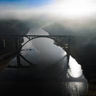 Za železobetonovým mostem vykukují z klidné hladiny pozůstatky starého mostu.