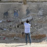 Umělec známý jako „syrský Banksy“ Bilál Šorba se po návratu z exilu vrátil do jedné ze zdevastovaných kolébek syrské revoluce – jediného města, které během téměř 14 let trvající občanské války přišlo o celé své obyvatelstvo. Byl překvapen, že některé z jeho děl přežily, popsal reportérům agentury AFP.

(Šorba si fotí kus zničené budovy, kam v roce 2016 namaloval své dílo „Symfonie revoluce“, které ukazuje tragický vývoj od nenásilného idealismu k neúprosné smrti – žena hraje na housle, zatímco ozbrojenci podporující i odmítající Asada na ni míří svými kalašnikovy.)