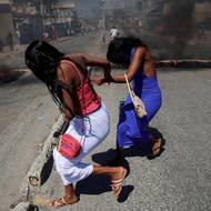 Ženy běží kolem hořících barikád ve čtvrti Solino, zatímco Haiťané volají o pomoc vládu a protestují proti nedostatečné bezpečnosti. (Port-au-Prince, 20. února)
