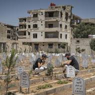 Dva muži se starají o hroby bojovníků zabitých během obléhání Daráji, 4. července. Na pozemku naproti, pod záhony dobře udržovaných keřů, leží hromadné hroby dosud neidentifikovaných obětí masakru z srpna 2012, kdy vládní síly a spojenecké milice řádily ve městě a za pouhé tři dny zabily 700 lidí.