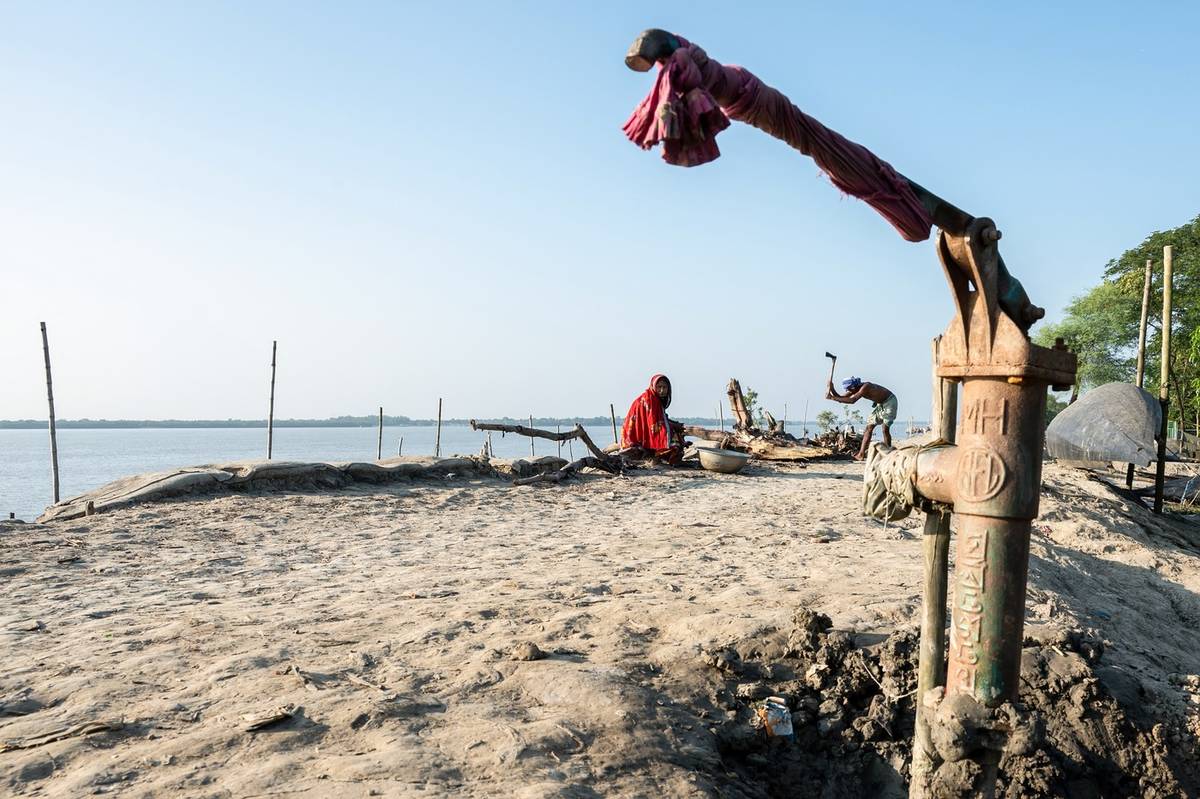 Na pobřeží Bangladéše, kde se mohutné himálajské řeky setkávají s mořem, určuje voda rytmus života. A také každý zápas. (Rybář zatlouká mrtvý strom vedle nefunkční ruční pumpy na břehu řeky Kholpetua v okrese Khulna, vyfoceno 20. října.)
