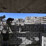 Nyní je dobrovolníkem v městské civilní správě a chce ukázat, že život jde dál, i v těchto nejistých podmínkách. V Daráji jsou rodiny, které se přistěhovaly zpět a usadily se v rozbořených domech.

(Syrští stavební dělníci opravují budovu v Daraji na předměstí Damašku, 29. října.)