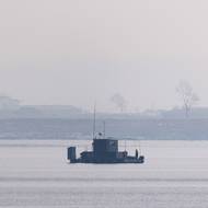 Člověk stojí na plovoucí vyhlídkové plošině se severokorejskou vlajkou na řece Jalu poblíž severokorejského města Sinuidžu, 11. března 2026.