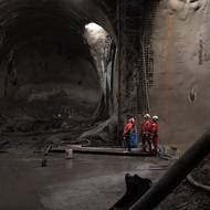 Dělníci v dočasné šachtě, která bude zasypána. V pozadí prochází traťový tunel směr Pankrác. Vpravo je vidět zárodek…
