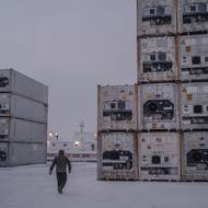 „Před deseti nebo patnácti lety pokryl led moře již v září, letos v zimě se tak stalo až koncem prosince a v lednu,“ řekl. (Muž prochází mezi řadami kontejnerů na cestě k trajektu Sarfaq Ittuk v přístavu Sisimiut, 14. března 2026.)