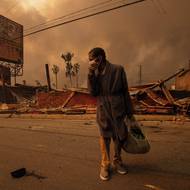 Zničeno bylo přes 18 000 budov, domov opustilo na 200 tisíc obyvatel. (Muž prochází kolem podniku zničeného požárem Eaton Fire, který silně zasáhl dělnické čtvrti. Tamních mnoho nedostatečně pojištěných majitelů domů čelí gentrifikaci a vystěhování, Altadena, 8. ledna 2025.)