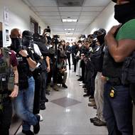 Agresivní praktiky ICE, spolu s extrémně přeplněnými a nehygienickými podmínkami v zadržovacích zařízeních, vyvolaly bouřlivé protesty a hromadné žaloby. (Maskovaní agenti čekají před soudními síněmi s fotografiemi hledaných, New York City, 8. července 2025.)