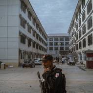 Voják Karenské národní osvobozenecké armády hlídkuje v areálu Shunda Park. Přibližně 900 čínských zaměstnanců zde po razii zůstalo několik týdnů zabarikádováno, protože se obávali, že repatriace by mohla vést k okamžitému zatčení čínskými úřady. (5. prosince 2025)