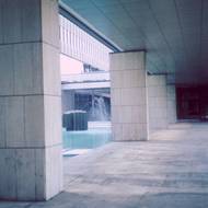 Pohled na atrium navržené jako centrální výtvarný i orientační prvek. Bylo řešeno jako kamenná zahrada s vodní plochou na oblázkovém podloží, záměrně bez zeleně. Masivní kamenné pilíře navázaly na materiál terasy (bílý travertin), představu zahrady dotvářely dvě monumentální kovové plastiky Věry Janouškové.