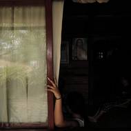 Fotografováním žen ve své širší rodině se Ospina snaží pochopit „tíhu absence“ a systémový i osobní dopad „neúplného dětství“.(Ospinova 20letá sestřenice María sleduje s babičkou Orfelinou televizi. V Ospinově rodině je 12 žen, včetně matek, sester a dcer, ale pouze tři dospělí muži. 9. prosince 2025.)