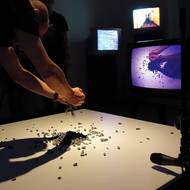 Tomáš Ruller: Živá smyčka, video‑akce / interaktivní video‑instalace, Klub Křenová, Brno, 1983. Televizor živě přenáší z kamery na stativu boční obraz akčního prostoru stolní desky, mikrofon na stojanu přes zesilovač a reproduktory zesiluje zvuk, k dispozici je kýbl se štěrkem, lopatka a malé koště, štěrk se opakovaně rozsypává a zase zametá.